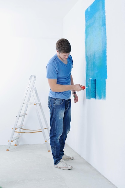 przystojny młody człowiek maluje w kolorze niebieskim i zielonym białą ścianę nowego domu
