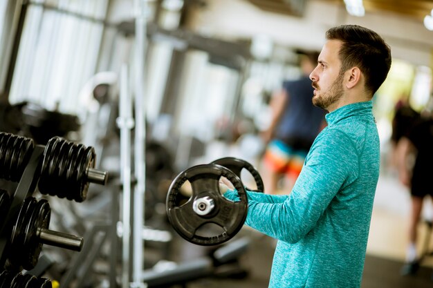 Przystojny młody człowiek używa dumbbells w gym