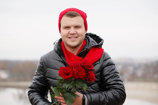 Przystojny młody człowiek z czerwonymi różami w rękach na zewnątrz w śnieżną pogodę