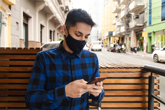 Przystojny młody człowiek z maską za pomocą swojego inteligentnego telefonu na ulicy.