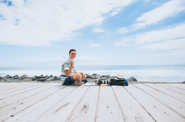 przystojny młody facet fotograf pracuje z laptopem na plaży