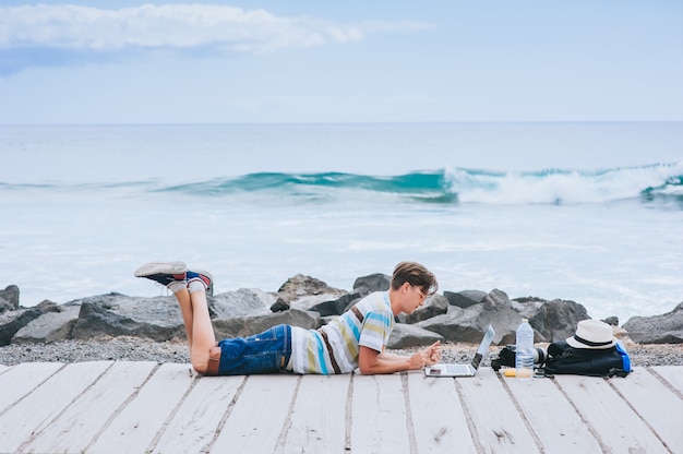 przystojny młody facet fotograf pracuje z laptopem na plaży