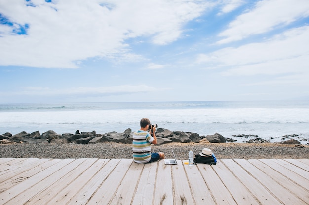 przystojny młody facet fotograf pracuje z laptopem na plaży