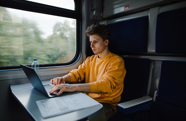 Przystojny młody freelancer mężczyzna pracuje na laptopie w pociągu siedzi przy stole