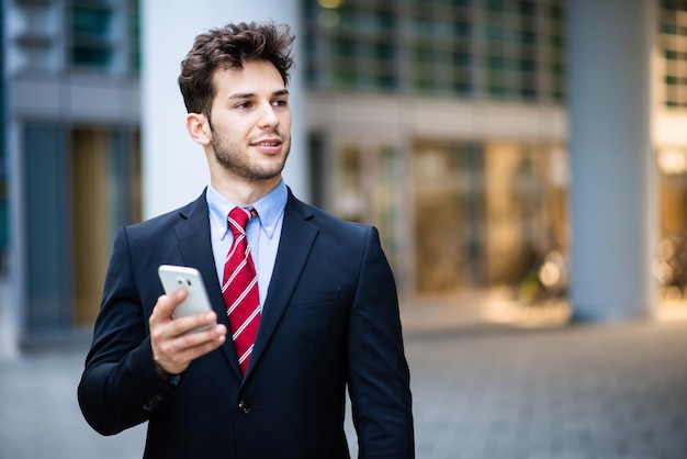 Przystojny młody kierownik używa smartphone plenerowego
