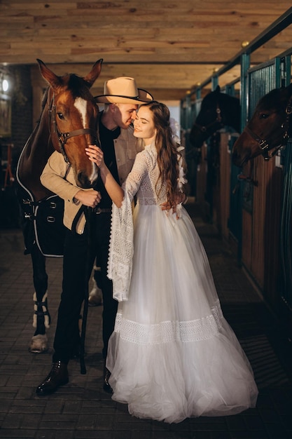 Przystojny młody kowboj i jego urocza panna młoda boho pozują w stajni z końmi