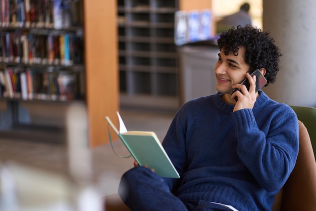 Przystojny młody latynoski student rozmawiający przez telefon komórkowy podczas relaksu w kampusie biblioteki