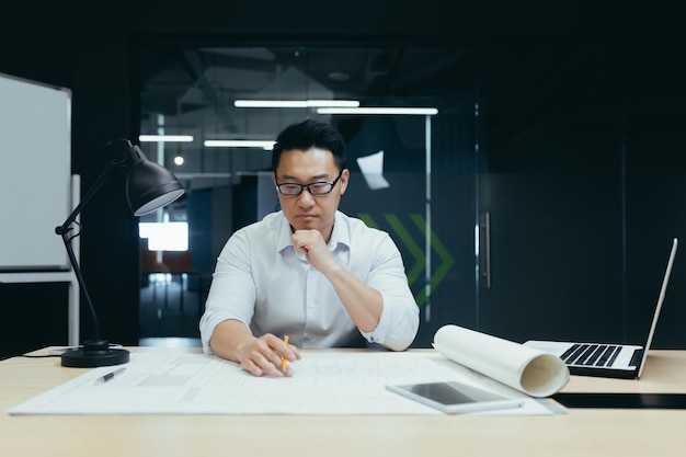 Przystojny młody mężczyzna, azjatycki architekt projektant, inżynier siedzi przy biurku w biurze przy stole