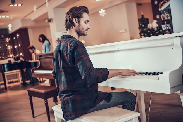 Przystojny młody mężczyzna gra na pianinie w sklepie instrumentów muzycznych