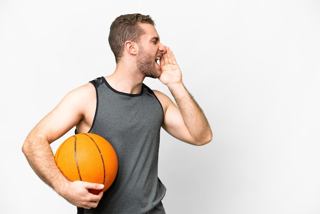 Przystojny młody mężczyzna gra w koszykówkę na białym tle, krzycząc z szeroko otwartymi ustami z boku