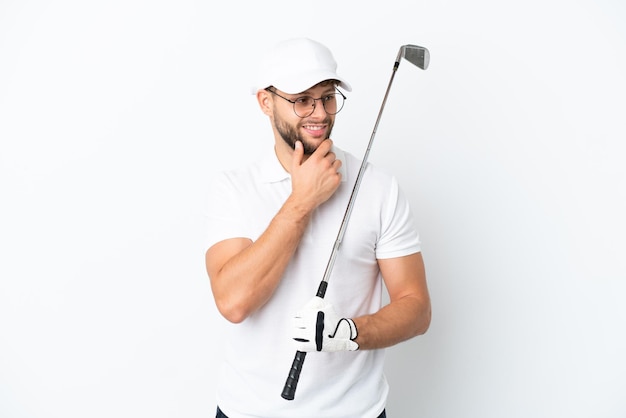 Przystojny młody mężczyzna grający w golfa na białym tle patrząc w bok i uśmiechnięty