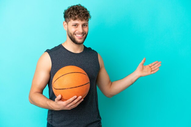 Przystojny młody mężczyzna grający w koszykówkę na białym tle na niebieskim tle wyciągając ręce do boku za zaproszenie do przyjścia