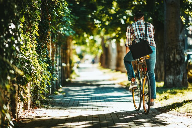 Przystojny młody mężczyzna jedzie do miasta na swoim rowerze. Jeździ na rowerze, zadowolony z ładnej pogody i spokojnej ulicy.