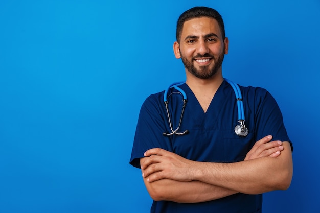 Przystojny młody mężczyzna lekarz w niebieskim mundurze ze stetoskopem na niebieskim tle