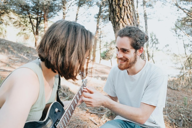 Przystojny młody mężczyzna nauczania hipster dziewczyna grać na gitarze na drzewach leśnych podczas zachodu słońca. Nauka nowej radosnej koncepcji umiejętności. Muzyka z miejsca na kopię. Młoda para gitara elektryczna