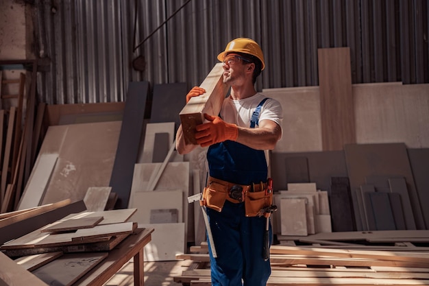 Przystojny młody mężczyzna niosący drewnianą deskę na budowie
