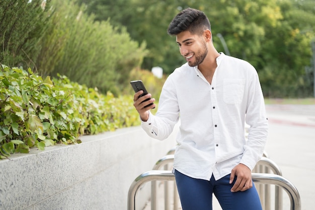 Przystojny młody mężczyzna rasy mieszanej uśmiechający się przy użyciu telefonu komórkowego na zewnątrz
