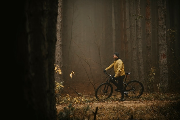 Przystojny młody mężczyzna robi sobie przerwę podczas jazdy na rowerze przez jesienny las