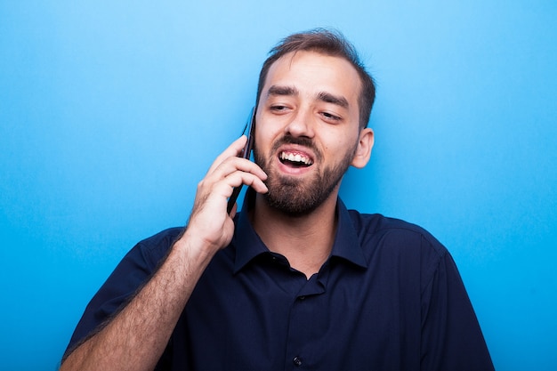 Przystojny młody mężczyzna rozmawia przez telefon na niebieskim tle w studio zdjęcie