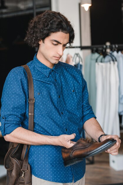 Zdjęcie przystojny młody mężczyzna trzymający skórzany but podczas zakupów w butiku