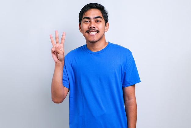Przystojny młody mężczyzna ubrany na co dzień w t-shirt pokazujący i wskazujący palcami numer trzy, uśmiechający się pewny siebie i szczęśliwy na białym tle