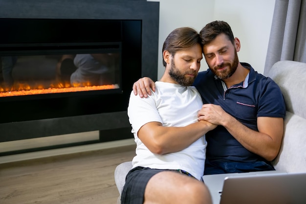 Przystojny młody mężczyzna używający notatnika i uśmiechający się, przytulając go kochającego chłopaka