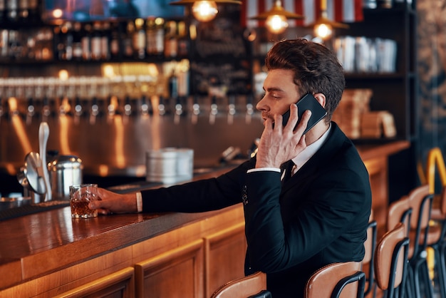 Przystojny młody mężczyzna w pełnym kolorze rozmawia na smartfonie siedząc przy barze w restauracji