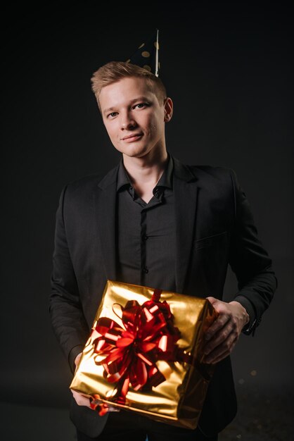 Przystojny młody mężczyzna w świątecznej czapce trzyma świąteczne pudełko z prezentem