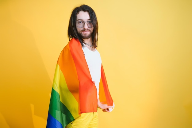 Przystojny młody mężczyzna z ruchem dumy LGBT Tęczowa flaga na ramieniu białym tle Mężczyzna z flagą dumy gejowskiej