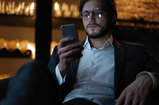 Przystojny młody mężczyzna za pomocą inteligentnego telefonu w nocy. Zbliżenie twarzy szczęśliwy biznesmen wiadomości na telefon komórkowy w nocy w kawiarni.