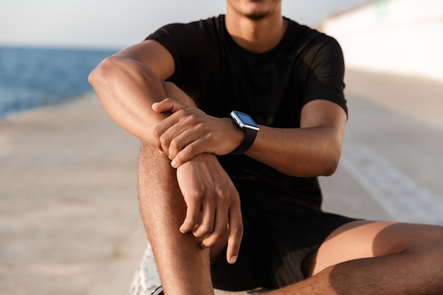 Przystojny młody sportowiec siedzi na świeżym powietrzu na plaży