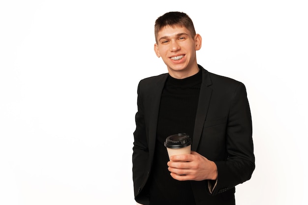 Przystojny młody uśmiechnięty mężczyzna w kurtce trzyma filiżankę kawy na wynos