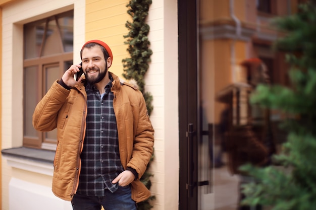 Przystojny modny hipster rozmawiający przez telefon komórkowy na zewnątrz