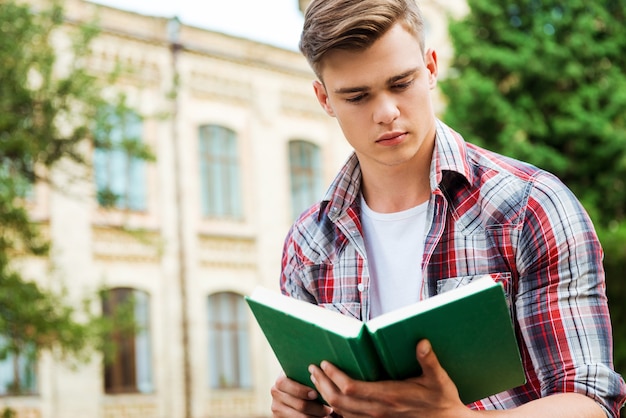 Przystojny Mól Książkowy. Przystojny Student Czytający Książkę Przed Budynkiem Uniwersyteckim