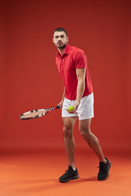 Przystojny muskularny sportowiec pozuje do aparatu fotograficznego na białym tle na czerwonym tle