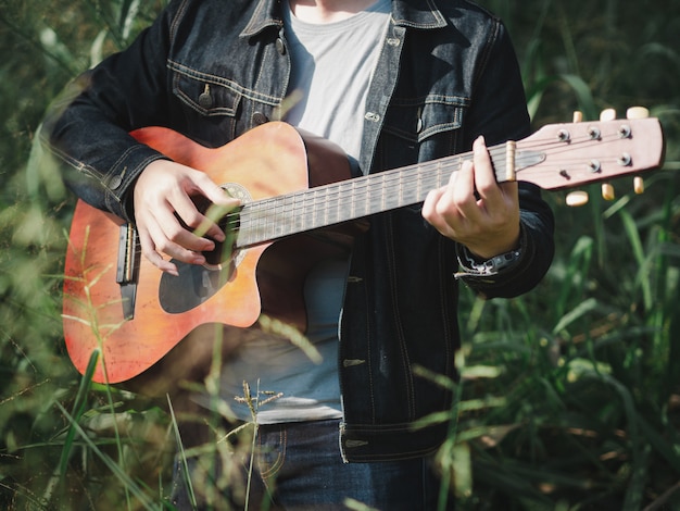 Przystojny Muzyk Bawić Się Gitarę Akustyczną Przy Trawy Pola Plamy Tłem.