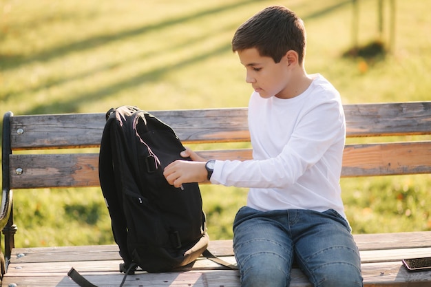 Przystojny nastoletni chłopak bierze z plecaka powerbark do ładowania smartfona Cute boy w parku jesienią