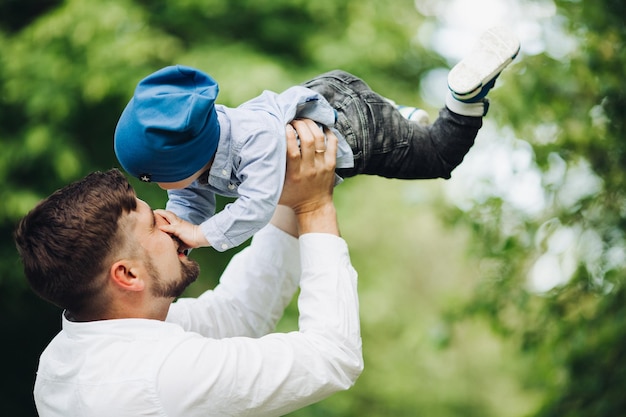 Przystojny ojciec rzuca chłopca przed letnim parkiem Mały chłopiec ubrany w stylowe ubrania i tata spędzający czas razem uśmiechając się i bawiąc się na zewnątrz w naturze Koncepcja szczęśliwego rodzicielstwa