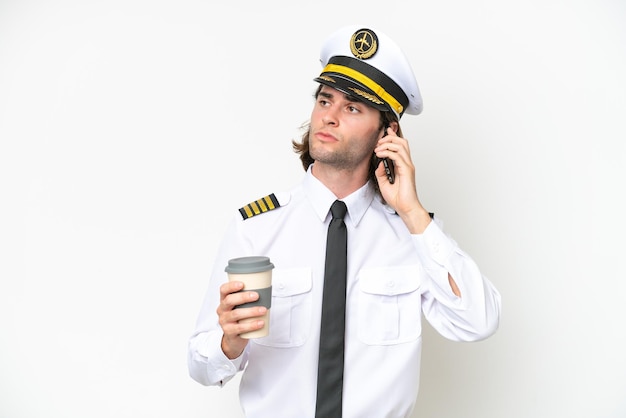 Zdjęcie przystojny pilot samolotu na białym tle trzymający kawę na wynos i telefon komórkowy