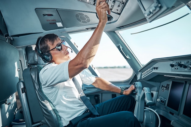 Przystojny pilot w okularach i słuchawkach siedzi w samolocie za sterem i przygotowuje się do odlotu