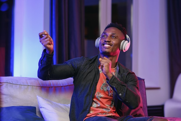 Przystojny, radosny 30-letni czarnoskóry facet słuchający młodzieńczych piosenek w słuchawkach na tle domowym