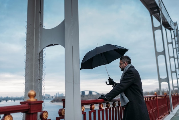 Przystojny samotny mężczyzna z parasolem stojącym na moście