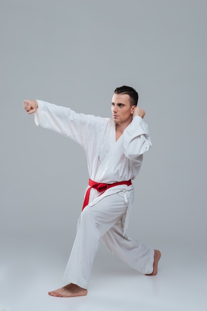 Przystojny sportowiec ubrany w praktykę kimono w karate na białym tle nad szarym tłem. Patrząc na bok.