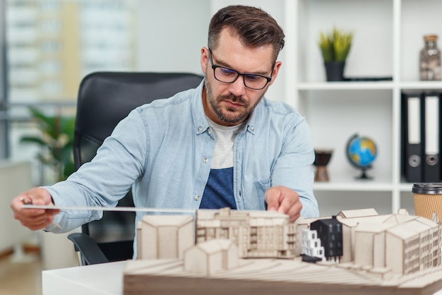 Zdjęcie przystojny starszy architekt kaukaski przy okularach pracuje nad projektem budowlanym i bada model, nad którym pracuje.