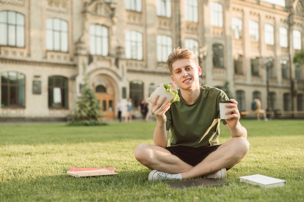 Przystojny student uniwersytetu je apetyczną kanapkę