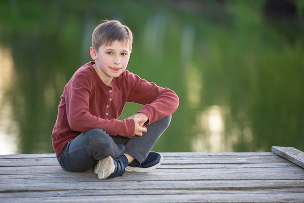 Przystojny szczęśliwy chłopiec siedzi na drewnianym moście