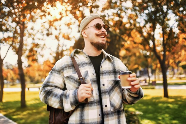 Przystojny Szczęśliwy Uśmiechnięty Brodaty Mężczyzna Pije Kawę Poza Ulicą Podczas Spacerów Po Parku Miejskim