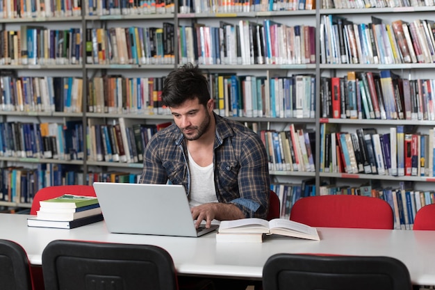 Przystojny uczeń z laptopem i książkami pracujący w bibliotece w liceum