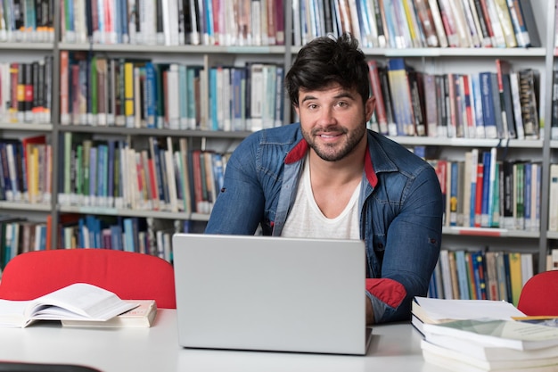 Przystojny uczeń z laptopem i książkami pracujący w bibliotece w liceum