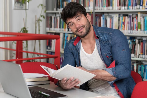 Przystojny uczeń z laptopem i książkami pracujący w bibliotece w liceum